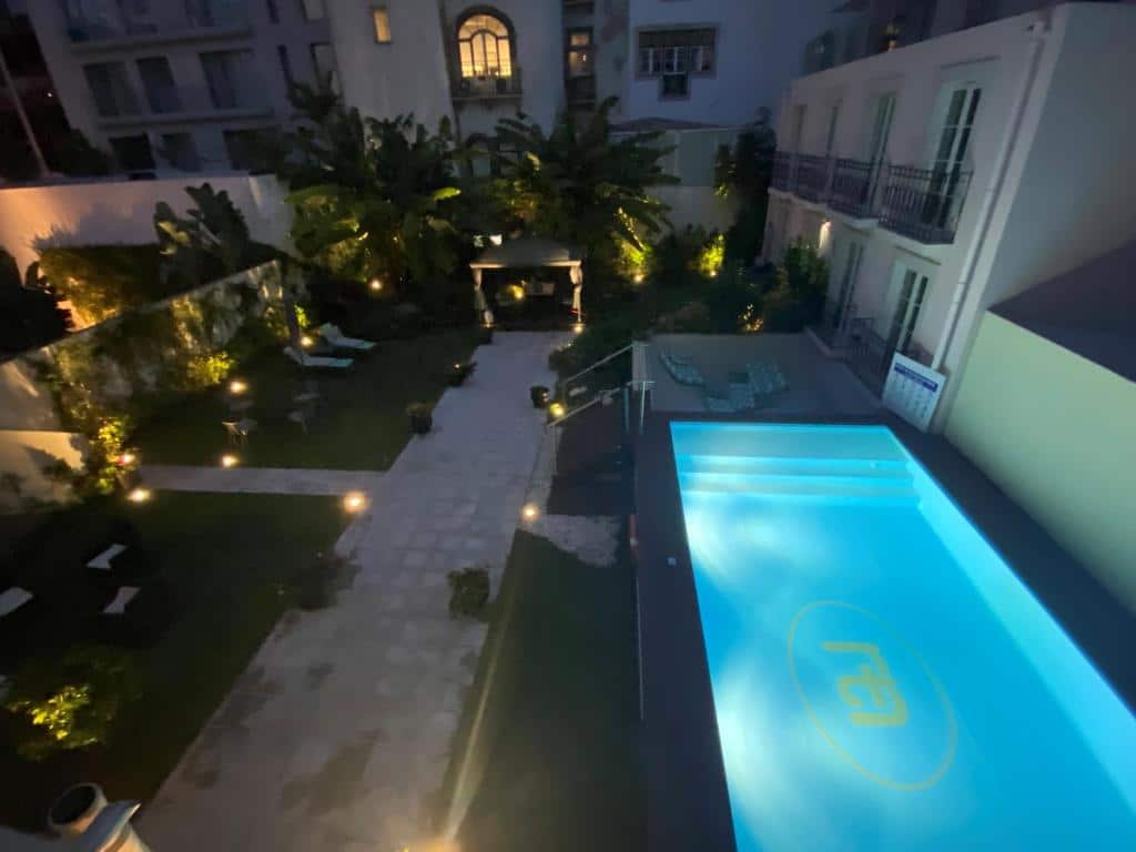 Vista aérea de um pátio com piscina iluminada, jardim, espreguiçadeiras e uma zona de estar coberta, à noite, no TM Luxury Apartments Lisbon.