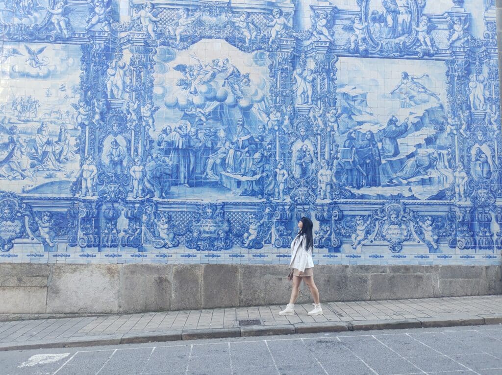 Mulher a caminhar numa rua do Porto com o mural de azulejos da Capela das Almas em fundo