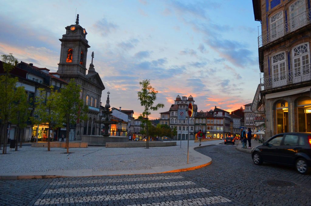 Praça de Guimarães ao pôr do sol, com edifícios históricos e ruas de calçada.