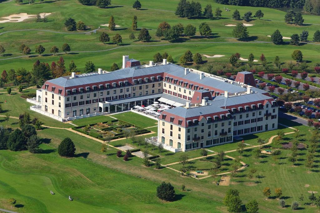 Um grande edifício em forma de U com um pátio, rodeado por jardins e campos de golfe, visto de cima. Este é o Radisson Blu Hotel Paris, Marne-la-Vallée, um dos hotéis perto da Disney Paris.