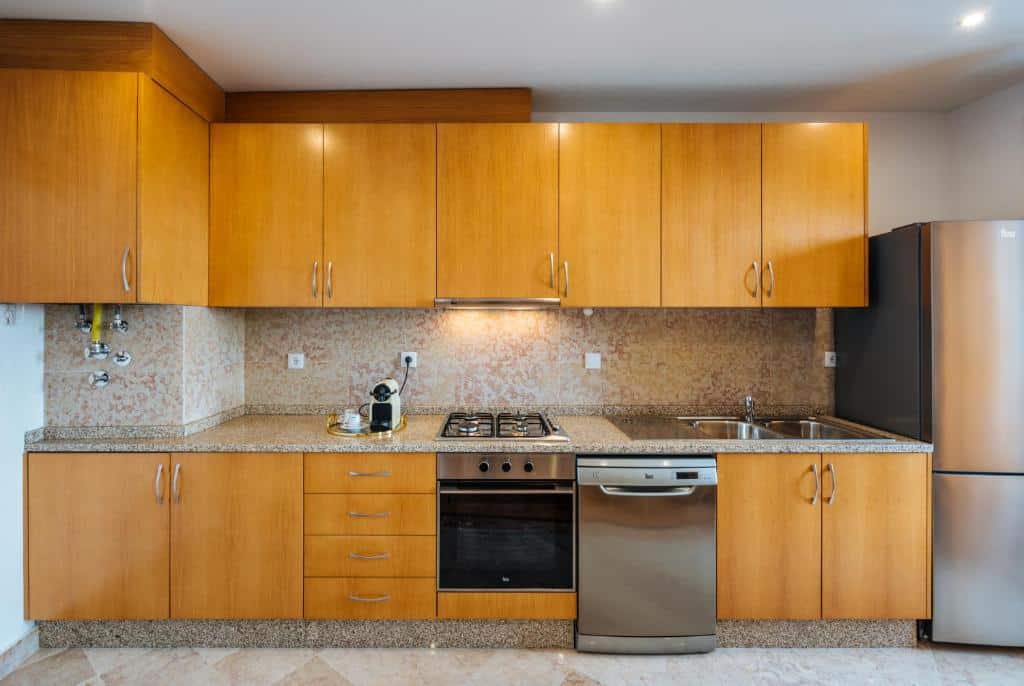 Cozinha do Varandas de Lisboa com armários de madeira, bancadas de granito, fogão, forno, máquina de lavar loiça e frigorífico em aço inoxidável.