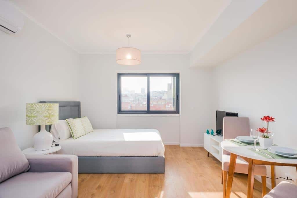 Apartamento estúdio moderno do 137 LuxResidence e iluminado com cama, poltrona, pequena mesa de jantar e uma janela com vista urbana.