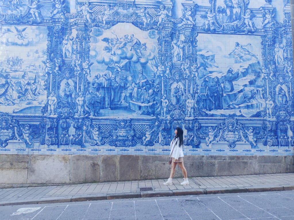 Uma pessoa vestida de branco em frente à Capela das Almas, no Porto, decorada com azulejos azuis e brancos.