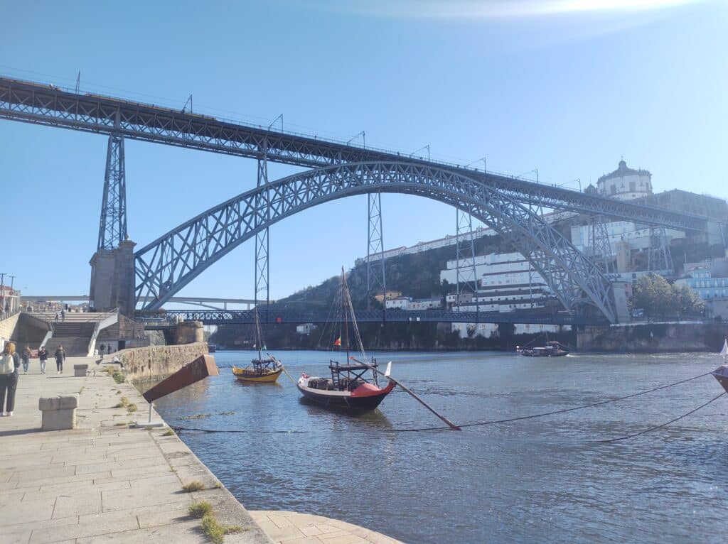 Ponte D. Luís I sobre o rio Douro, com barcos rabelos ao longo da margem