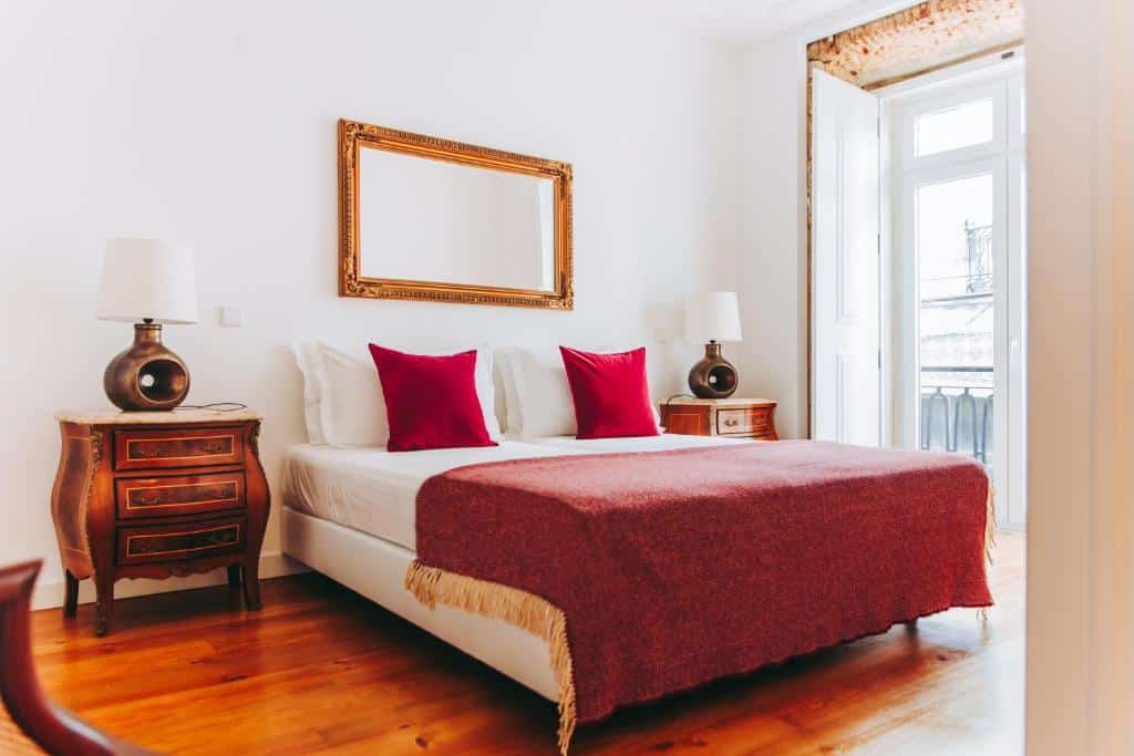 Quarto do 54 São Paulo com cama de casal, colcha vermelha e almofadas. Duas mesas de cabeceira de madeira com candeeiros e um grande espelho por cima da cama.