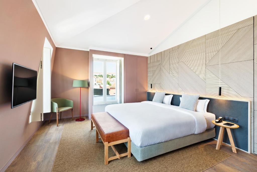 Quarto do OnJ S. Lázaro Lisboa com cama grande, TV na parede, chão de madeira e uma janela. Uma cadeira verde e um candeeiro de pé estão junto à janela.