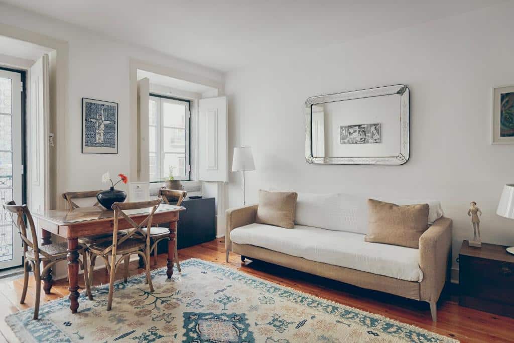 Sala de estar acolhedora da Casa dos Azulejos com um sofá bege, mesa de madeira com cadeiras, um grande espelho na parede e um tapete decorativo no chão.