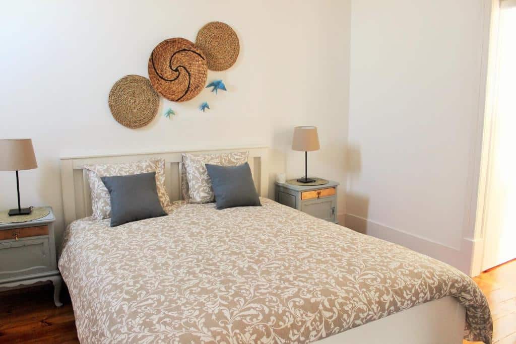 Quarto da Casa Rio da Saudade com colcha estampada, duas almofadas, duas mesas de cabeceira com candeeiros e decorações de tecido na parede.