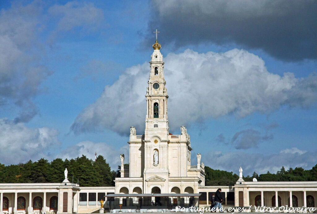 A Basílica de Nossa Senhora do Rosário, com uma torre alta e uma cruz, contra um céu azul com nuvens.