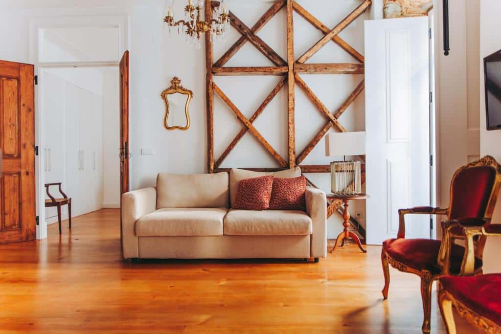 Sala de estar do 54 São Paulo com sofá bege, duas almofadas vermelhas, detalhes de madeira na parede, um candeeiro de teto e cadeiras de estilo vintage sobre chão de madeira.