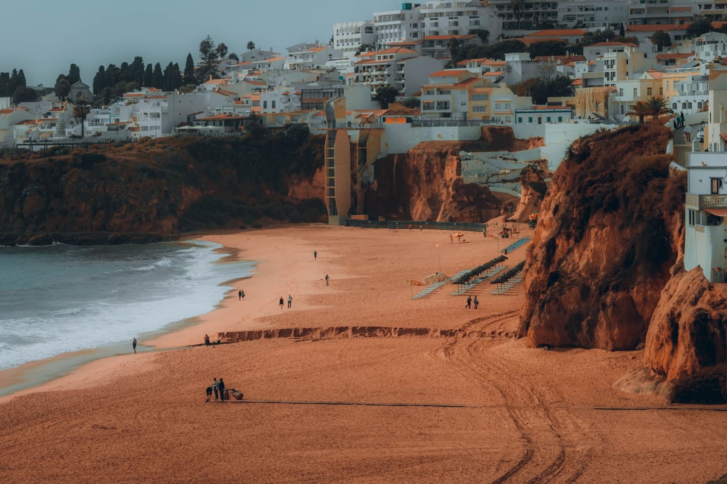 Praia de areia em Portimão com poucas pessoas, rodeada por falésias e edifícios brancos.