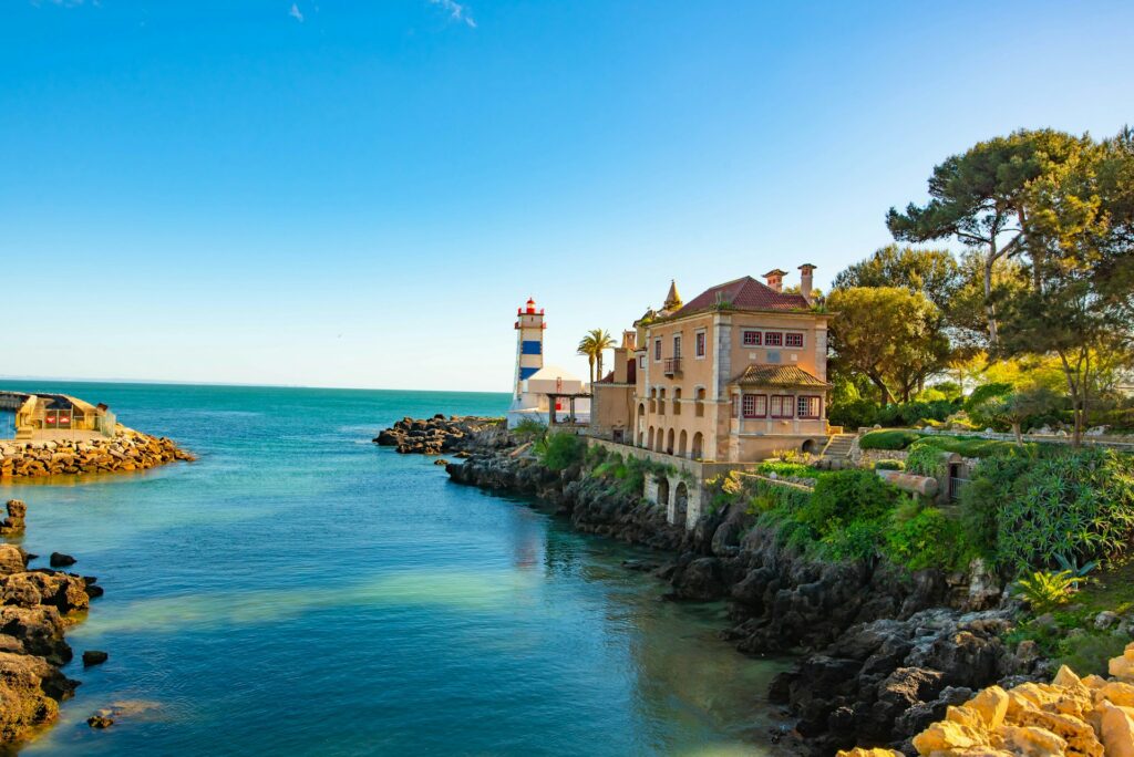 Mar junto ao Farol de Santa Marta, em Cascais, com uma casa ao lado do farol sobre rochas.