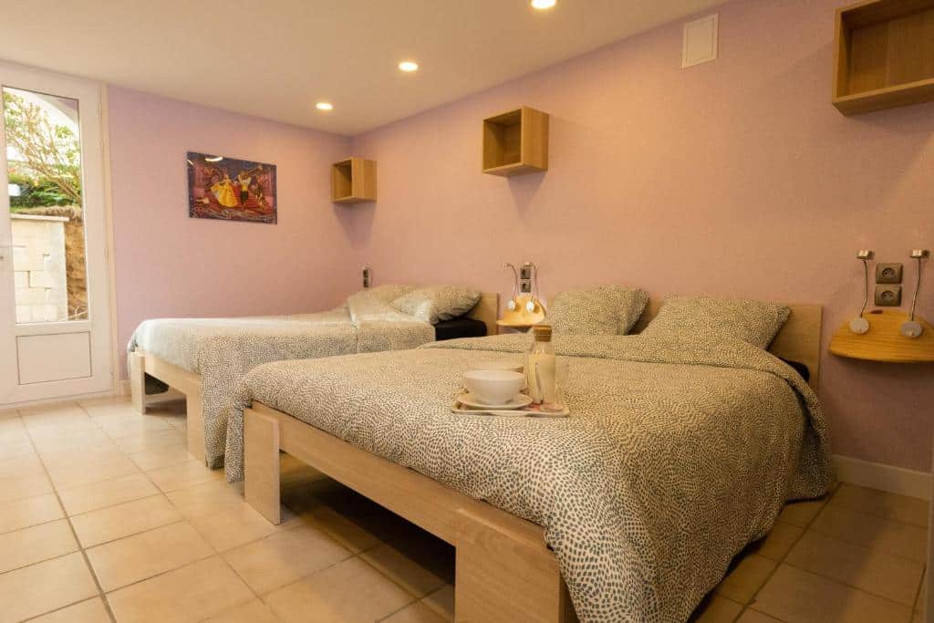 Um quarto do Les Chambres D'Aline, um dos hotéis perto da Disney Paris, com duas camas, roupa de cama estampada, prateleiras na parede, um candeeiro e uma bandeja com uma chávena sobre a cama.