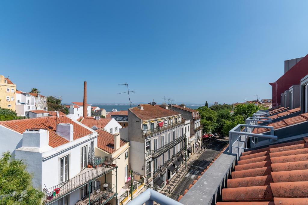 Vista do terraço do Portas do Céu sobre uma paisagem urbana com telhados vermelhos, uma grande chaminé e um rio ao fundo, sob um céu azul claro.