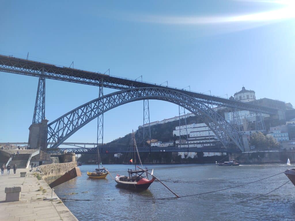 Ponte D. Luís I durante o dia, com barcos no rio e a ponte ao fundo.
