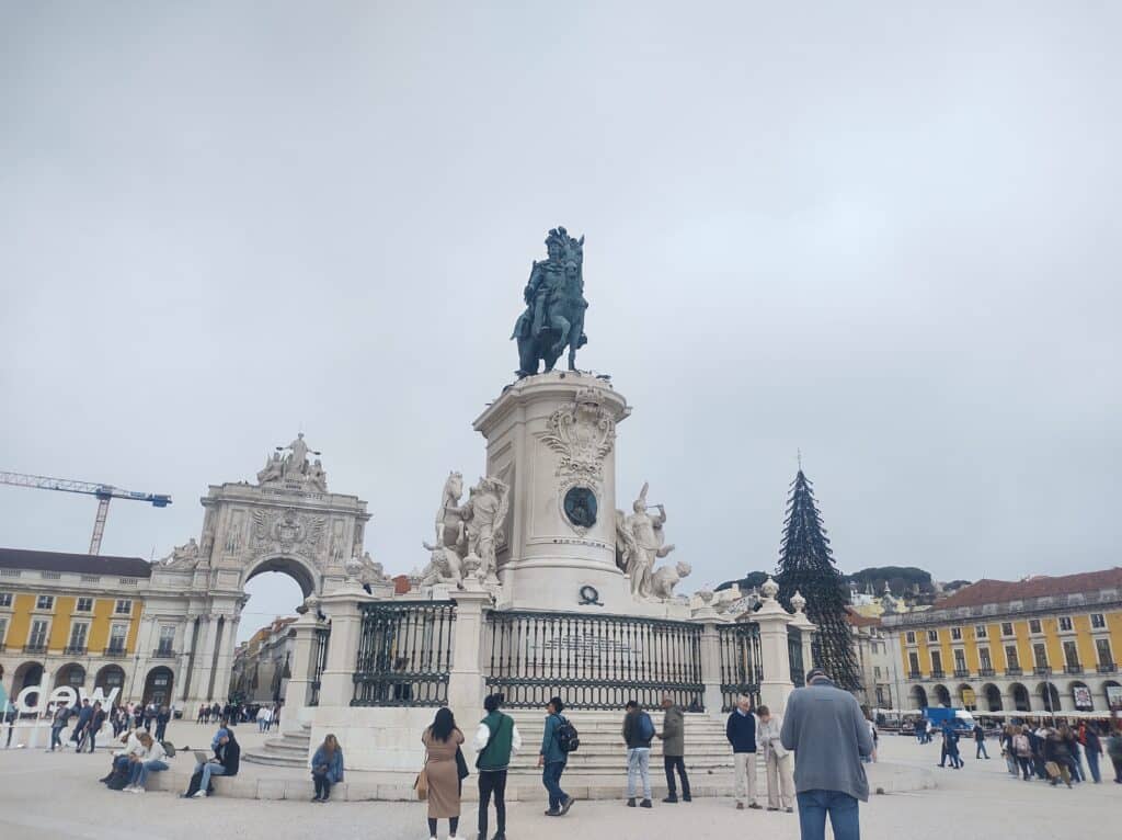 Imagem da Praça do Comércio, com uma estátua equestre ao centro, durante o dia.