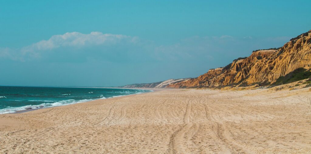 Praia de areias douradas, mar em tons de azul e costa suave na Costa Alentejana, no Alentejo.