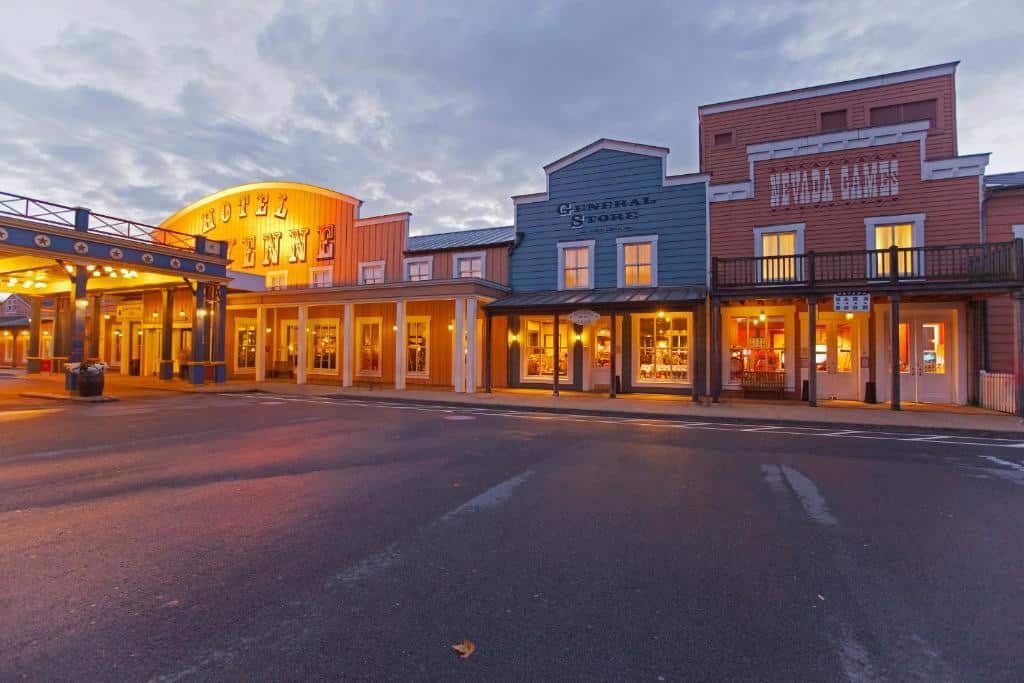 Edifícios em estilo do oeste americano, com fachadas de madeira e letreiros iluminados, ao anoitecer. Este é o Disney's Hotel Cheyenne, um dos hotéis perto da Disney Paris.