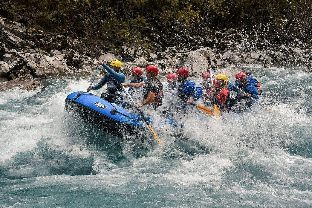 Um grupo de pessoas com capacetes pratica rafting num bote insuflável azul, navegando por rápidos rochosos no rio Tara, no Montenegro.
