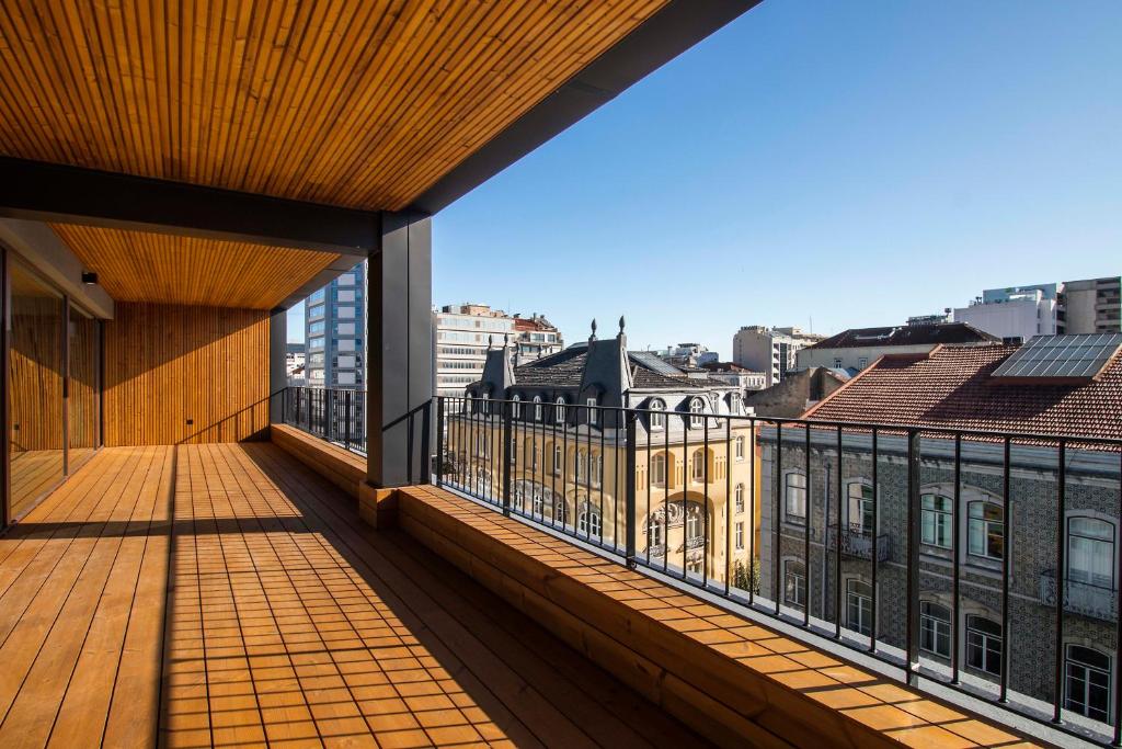 Amplo terraço de madeira com grades do Nôma Living Pop Saldanha, com vista para uma paisagem urbana com vários edifícios sob um céu azul claro.