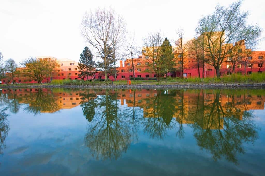 Uma fila de edifícios vermelhos e laranja com árvores, refletidos num plano de água calmo num dia claro, no Disney's Hotel Santa Fe, um dos hotéis perto da Disney Paris.