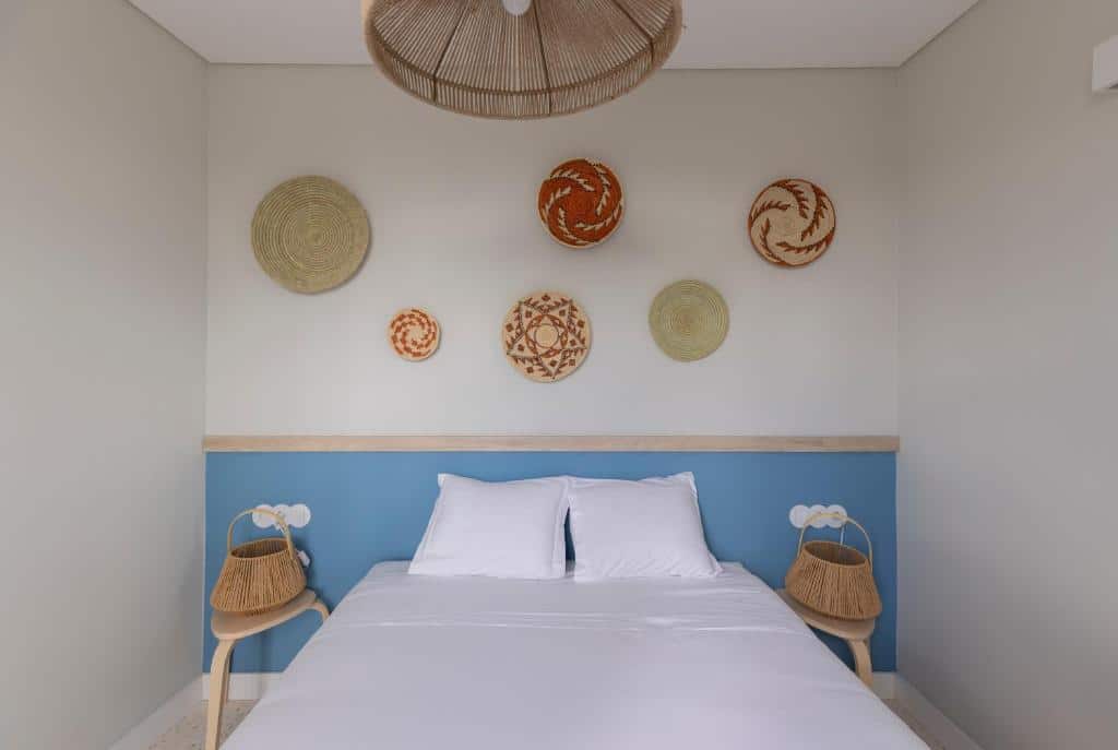 Cama do Líbere Lisbon Príncipe Real bem feita, com lençóis brancos; cestos de vime pendurados como decoração na parede. Dois candeeiros de vime nas mesas de cabeceira.