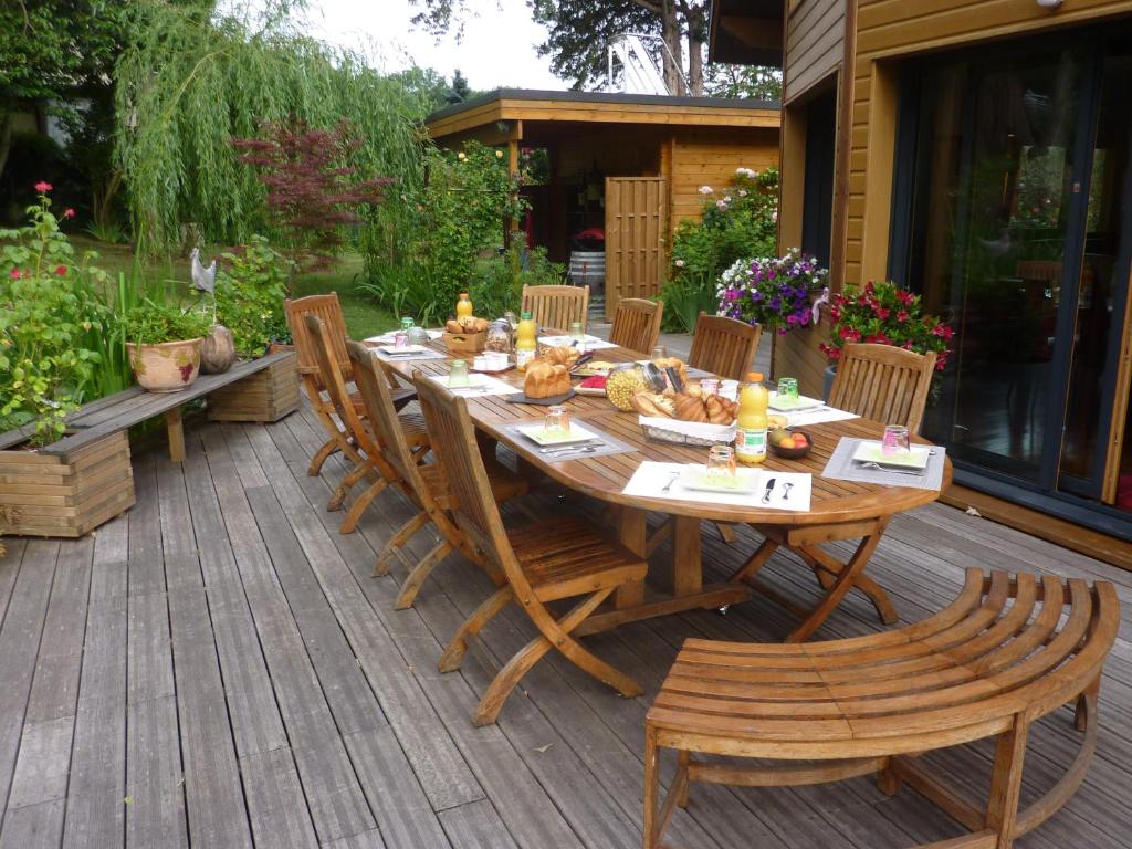 Uma mesa de jantar exterior, em madeira, posta para uma refeição, com oito cadeiras num deck de madeira, rodeada por plantas e flores no Les Chambres D'Oriane, um dos hotéis perto da Disney Paris.